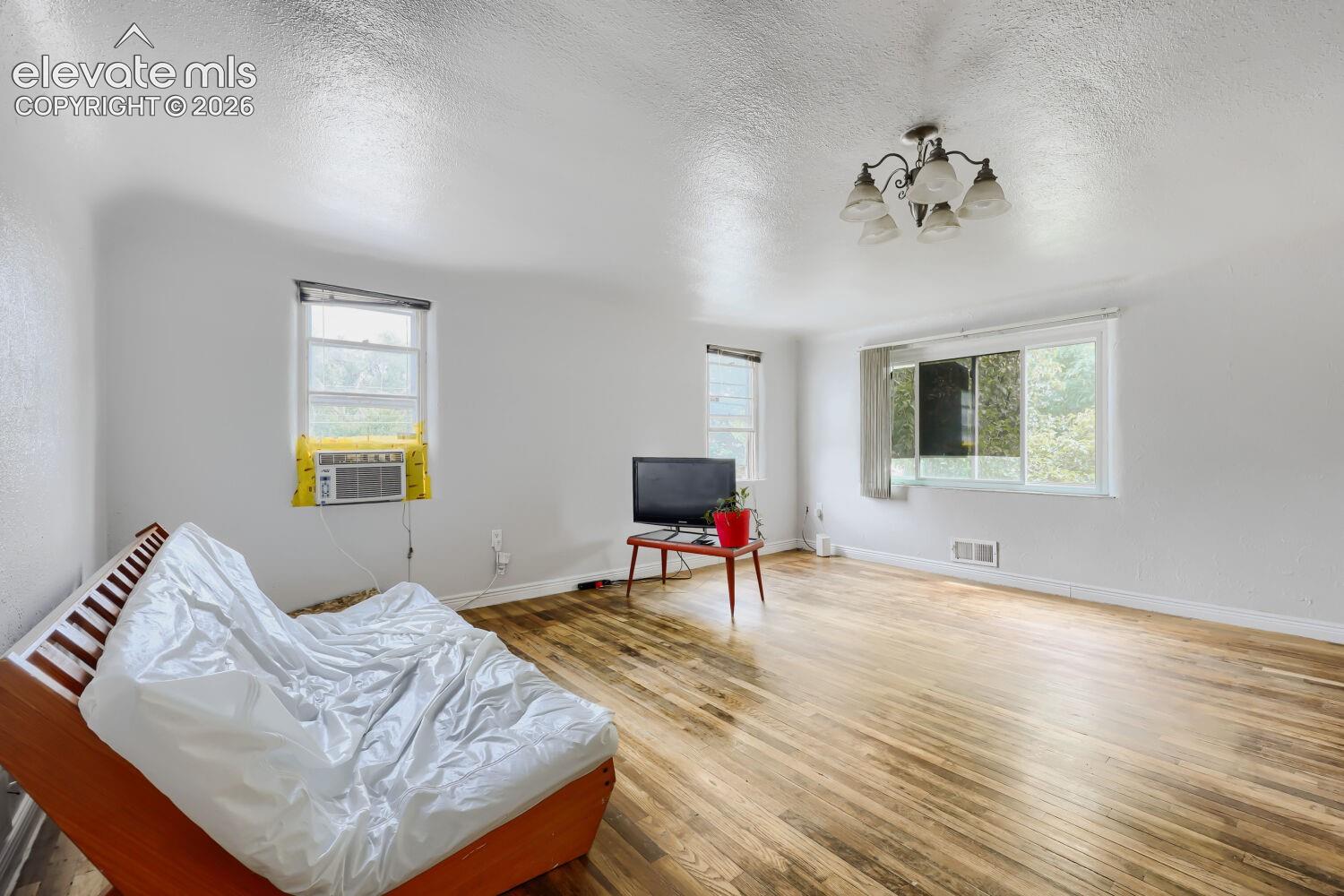 Hardwood flooring throughout, multiple windows providing ambient light, and a ceiling-mounted chandelier