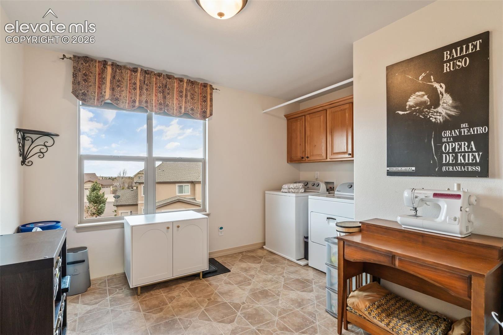 Dedicated laundry area featuring a large window, tiled flooring, wood cabinetry, built-in shelving, and a hanging rod