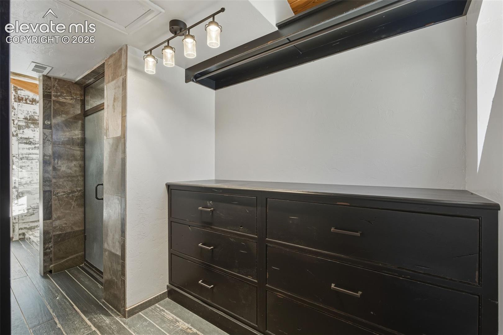 Built-in dark wood-finish dresser with dark metal pulls, integrated shelving, and track lighting