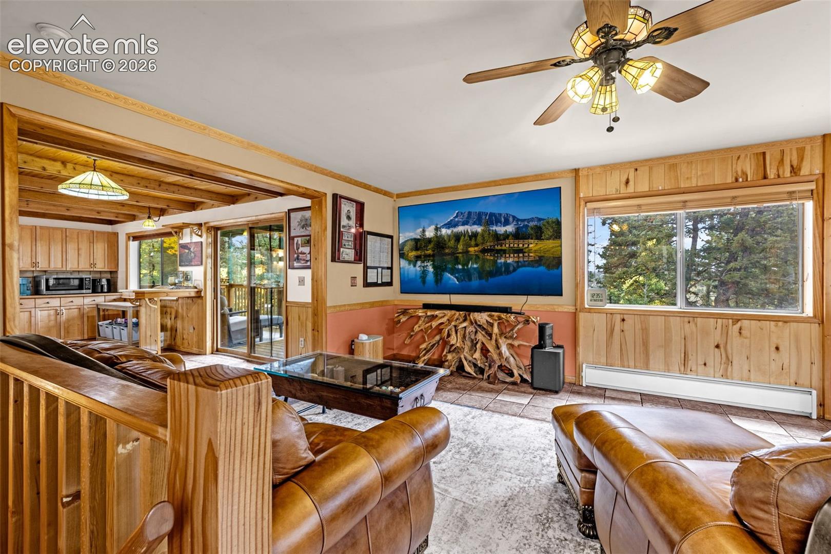 Open-concept interior featuring knotty pine wall paneling, crown molding, tile flooring, and a multi-blade ceiling fan with integrated lighting