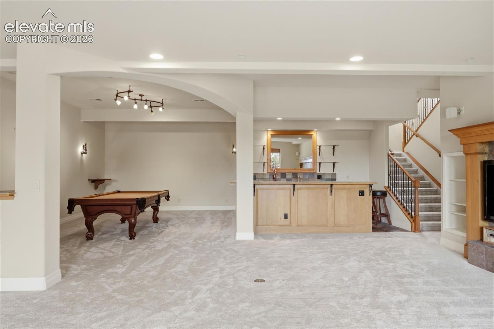 Lower level featuring light gray carpeting, a built-in wet bar with light wood cabinetry, a tiled backsplash, and an integrated sink