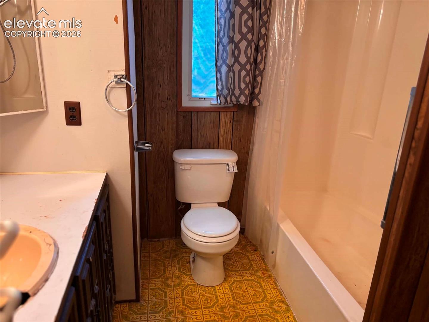 Bathroom featuring a white composite tub and shower surround, wall-mounted circular towel ring, integrated vanity sink, and patterned resilient flooring