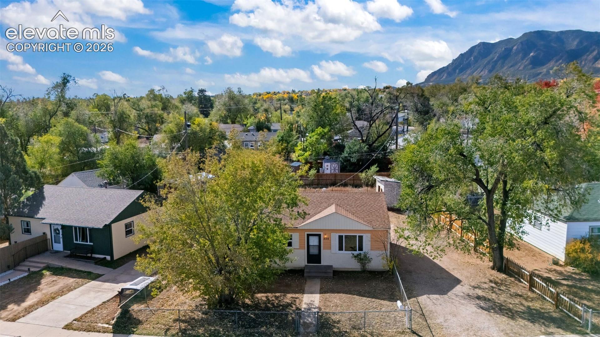 Single-story residence featuring a shingled roof, neutral-toned siding, a concrete walkway, and a chain-link fenced perimeter, set against a backdrop of mountain scenery
