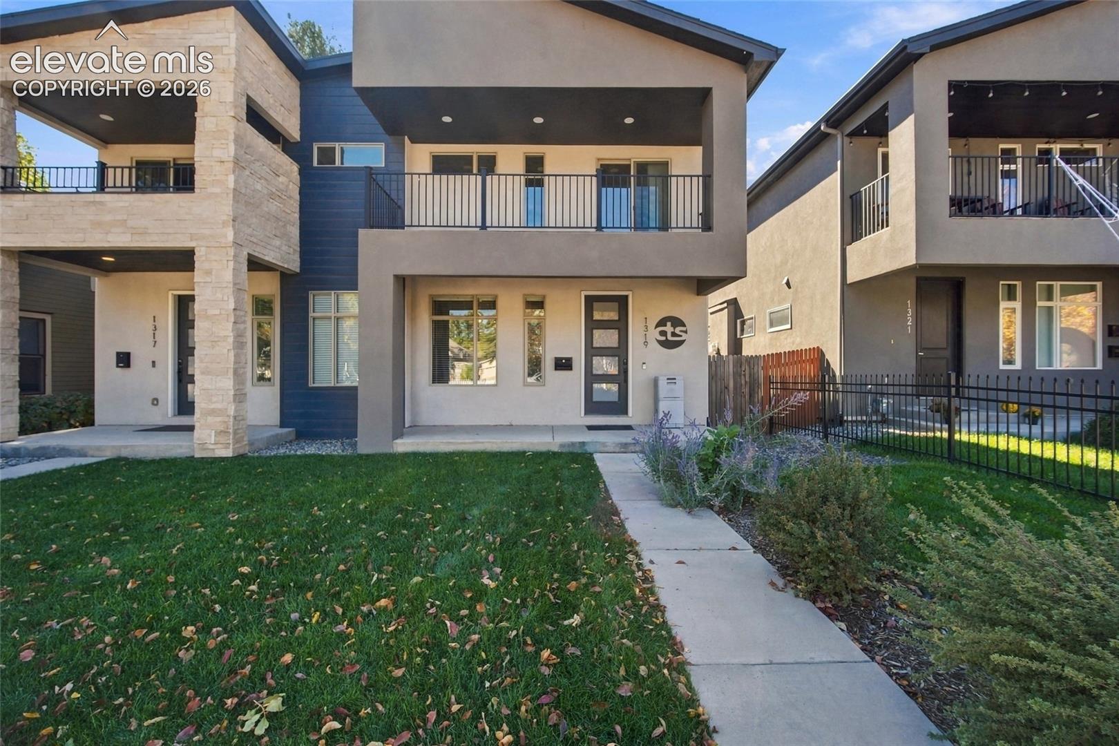 Modern multi-level exterior featuring stucco and stone facade, private second-story balconies, and black metal railings