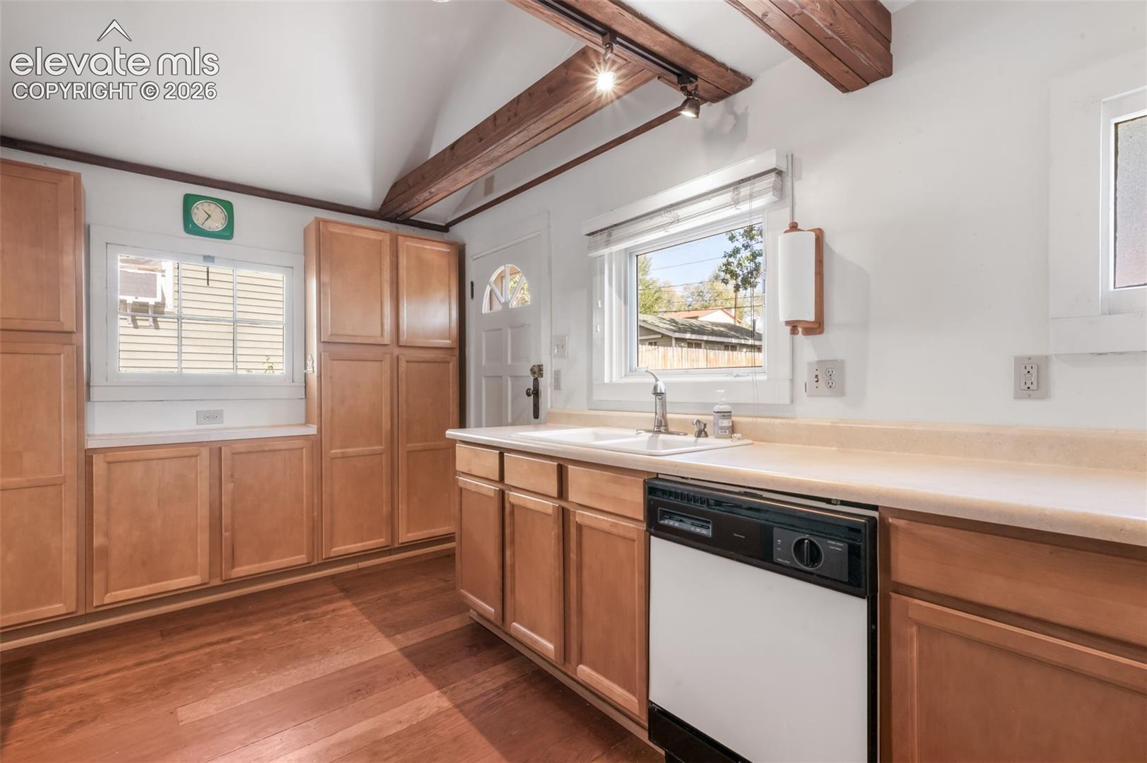Kitchen featuring wood-finish flooring, exposed ceiling beams, natural wood cabinetry, a white single basin sink, and a dishwasher