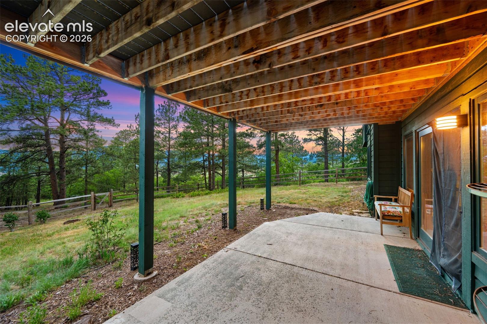 Covered concrete patio with exposed wood ceiling beams and a natural wood fence framing the landscape
