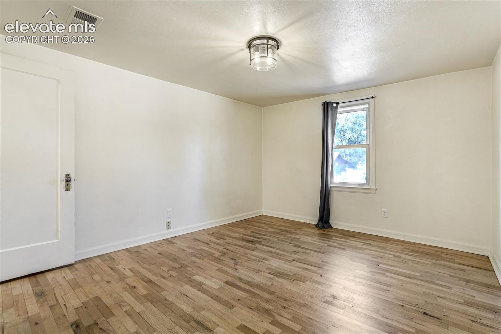 Room featuring wood-finish flooring, a single-pane window, and a flush-mount drum ceiling light