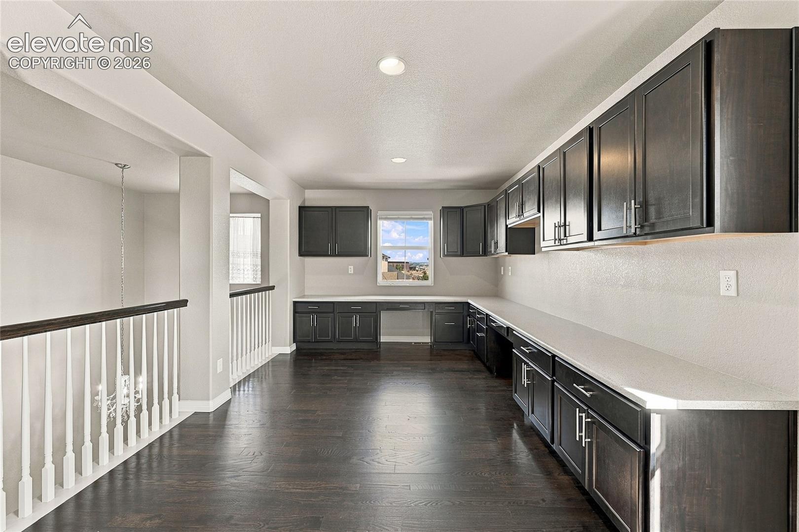 Built-in cabinetry featuring dark wood-finish, light-toned countertops, wood-finish flooring, recessed lighting, and a balustrade with a wooden handrail