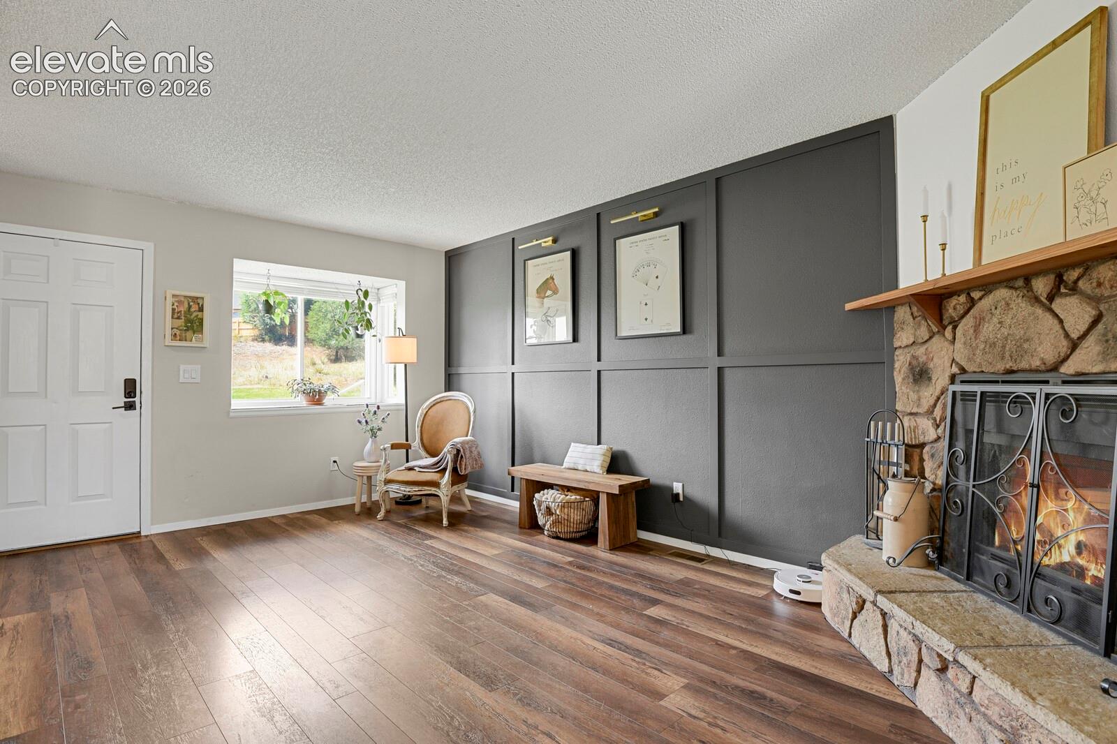 Stone-clad fireplace with a wood mantel, wood-finish flooring, and a decorative paneled accent wall