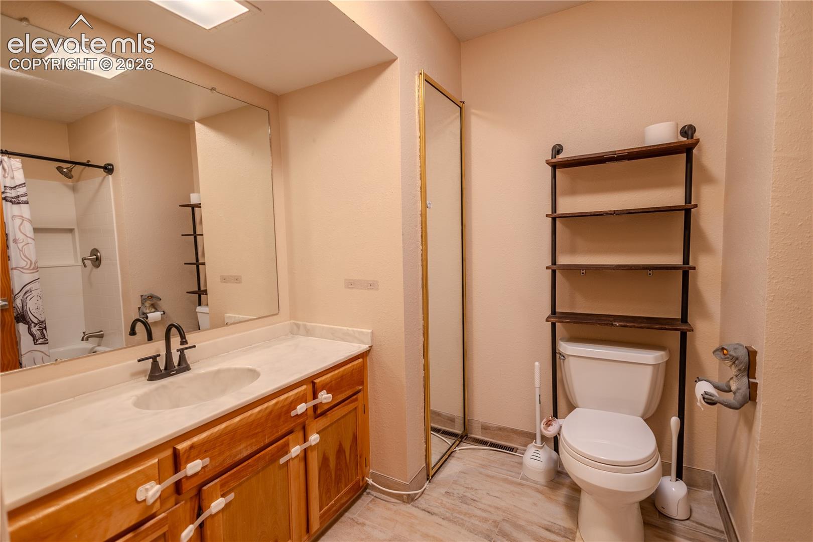 Full-width vanity with integrated sink and stone-finish countertop, wood cabinetry, large vanity mirror, tub-shower combination with recessed wall niche, and tile-finish flooring