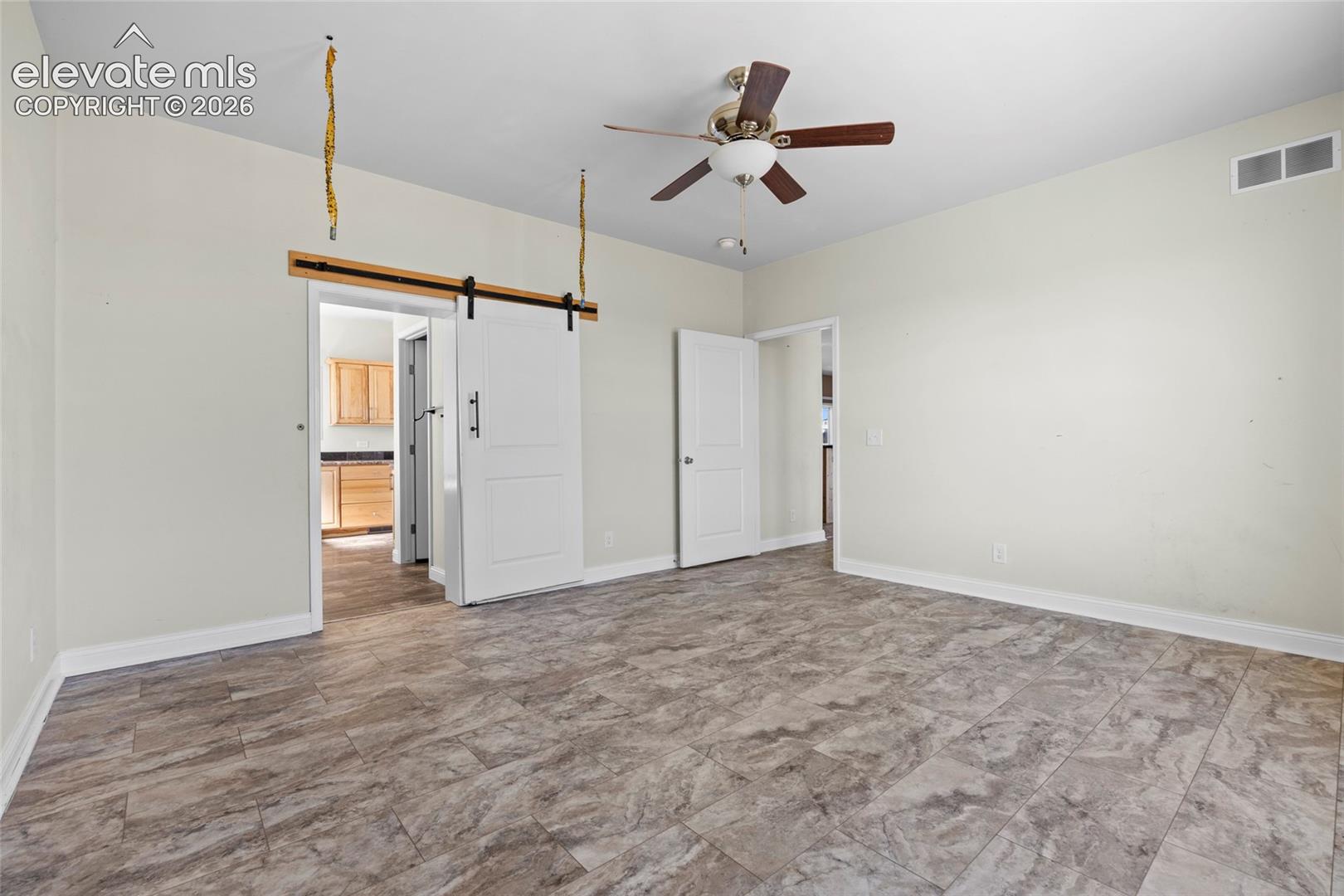 Interior room featuring patterned tile flooring, a ceiling fan with integrated lighting, a sliding door with a black hardware rail system, and standard swing doors