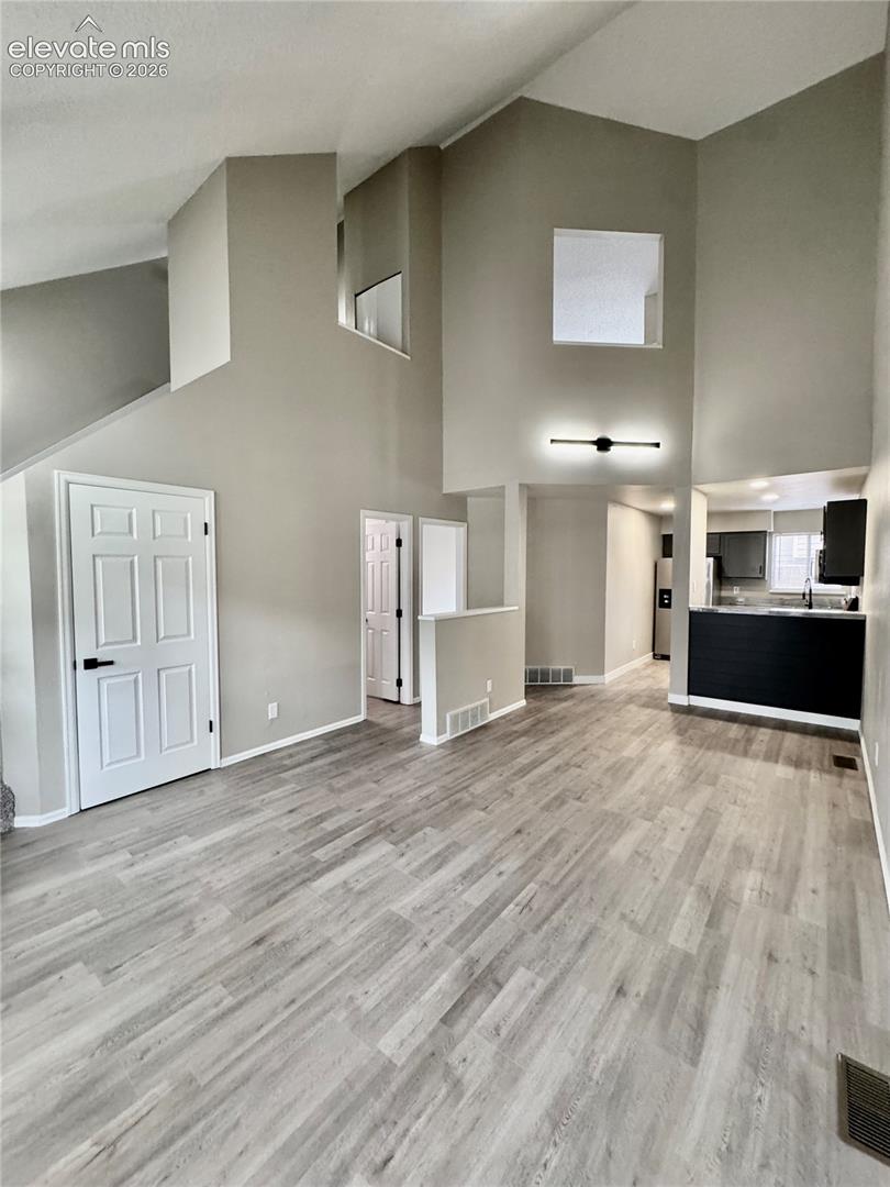 Vaulted ceilings with architectural wall cut-outs, gray wood-finish flooring, and a modern linear wall sconce