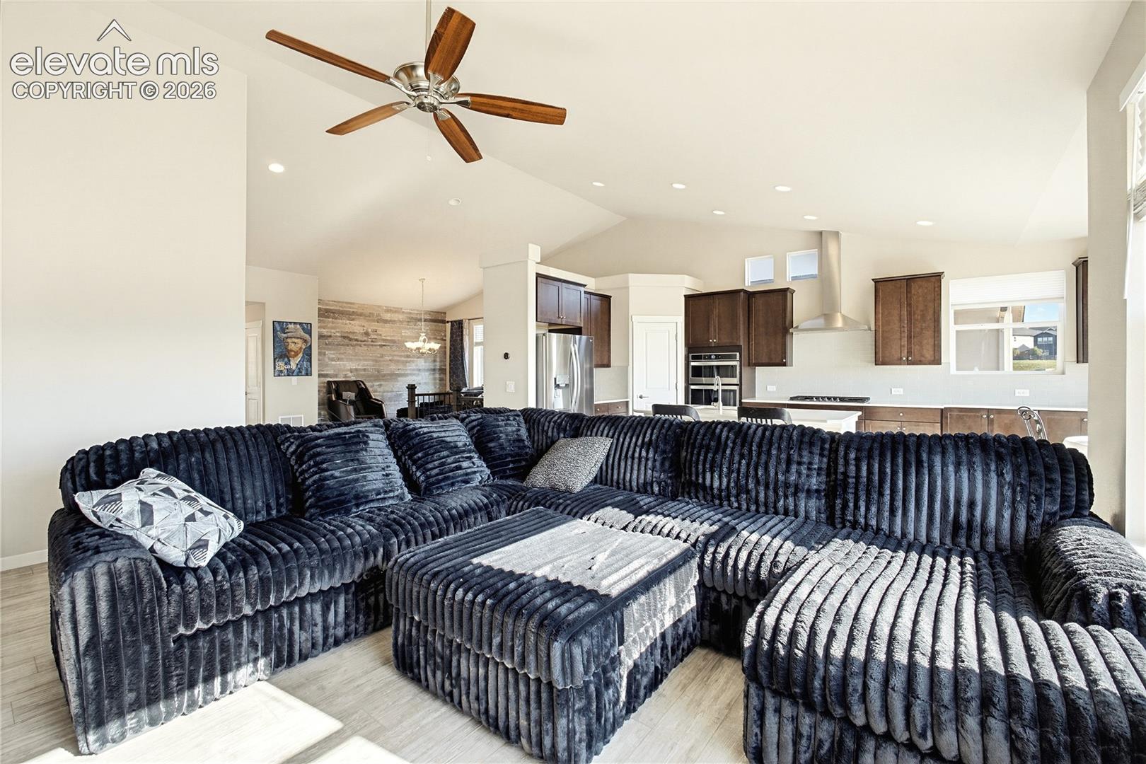Vaulted ceilings, recessed lighting, wood-finish flooring, and a kitchen featuring stainless steel built-in appliances with a wall-mounted range hood