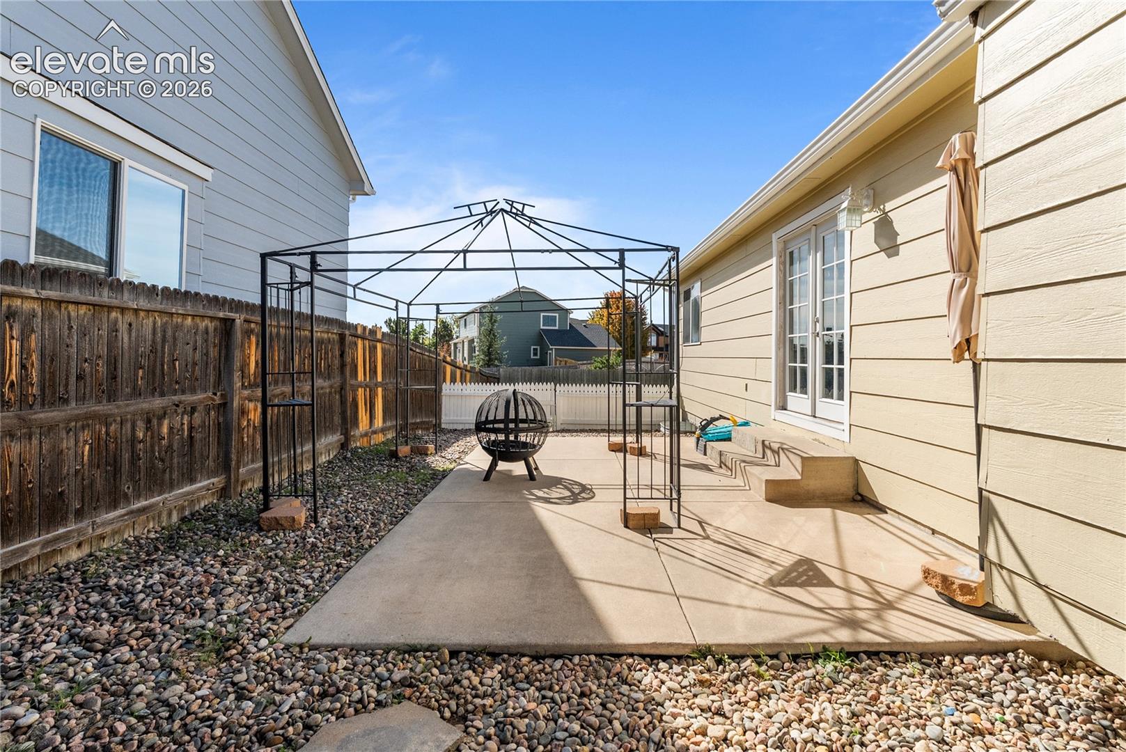 Concrete patio with metal gazebo frame, gravel landscaping, and wood privacy fence