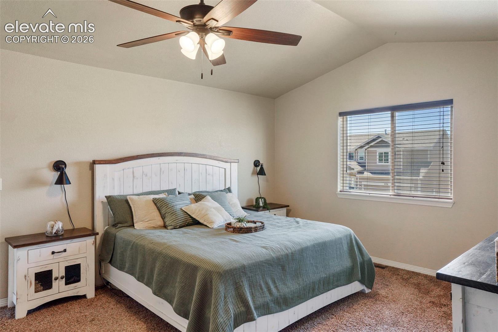 Vaulted ceiling featuring a ceiling fan with integrated lighting, a large window with blinds, and neutral-toned wall finishes