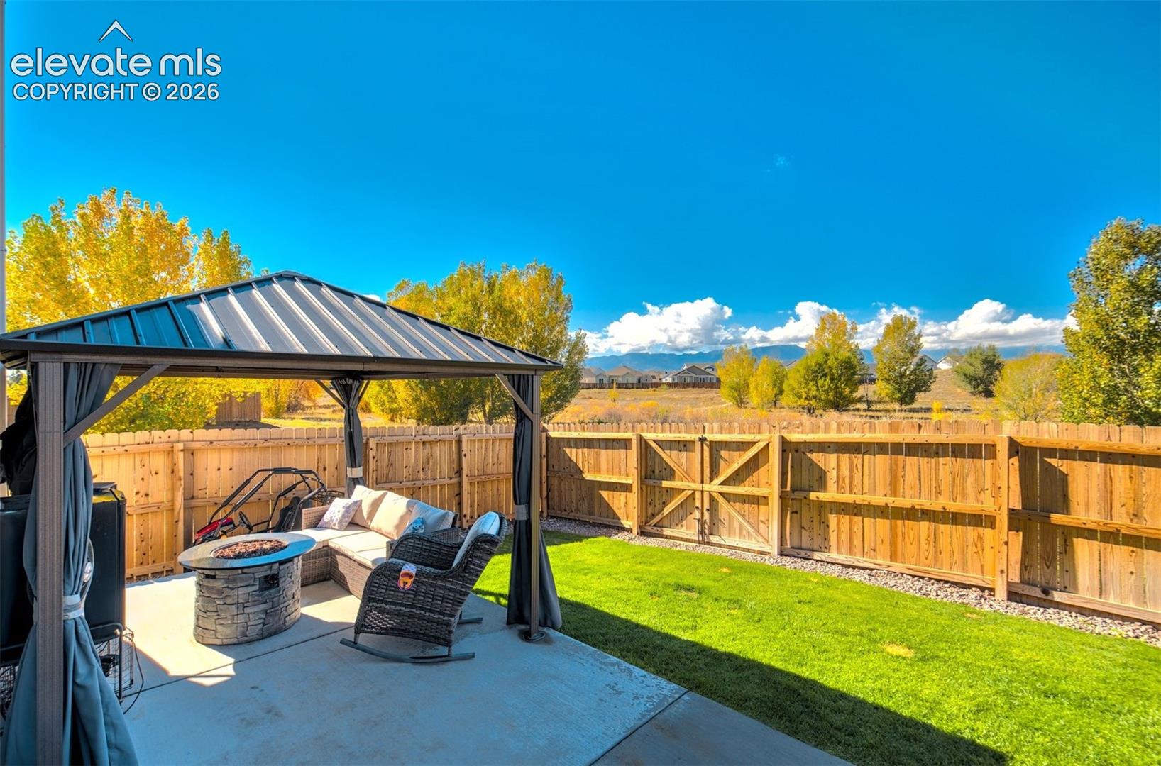 Backyard featuring a metal-roof gazebo, concrete patio, grass lawn, and wooden privacy fencing