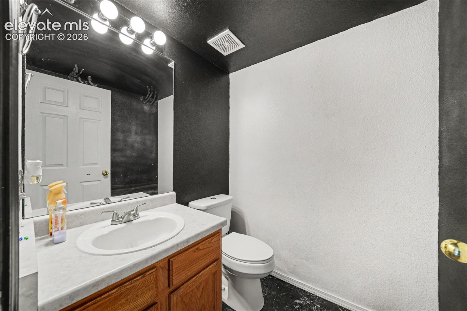 Bathroom featuring a wood-finish vanity with a stone-composite countertop, integrated oval sink, wall-to-wall mirror, and four-light fixture