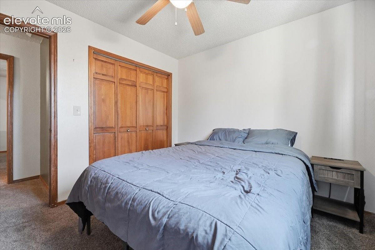 Wood-finish bi-fold closet doors, textured ceiling, and a ceiling fan