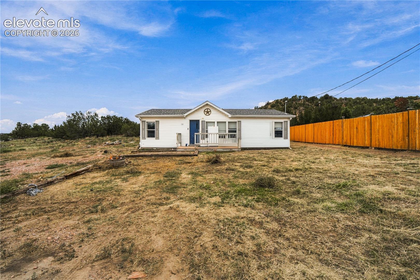White exterior siding with a blue entry door, a covered porch, and a wood privacy fence