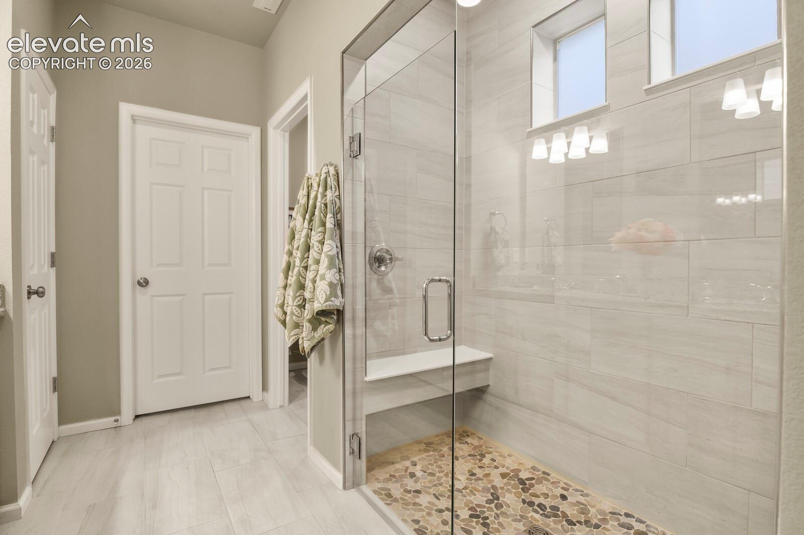 Walk-in shower featuring glass paneling, floor-to-ceiling tile surround, pebble-stone flooring, and a built-in bench