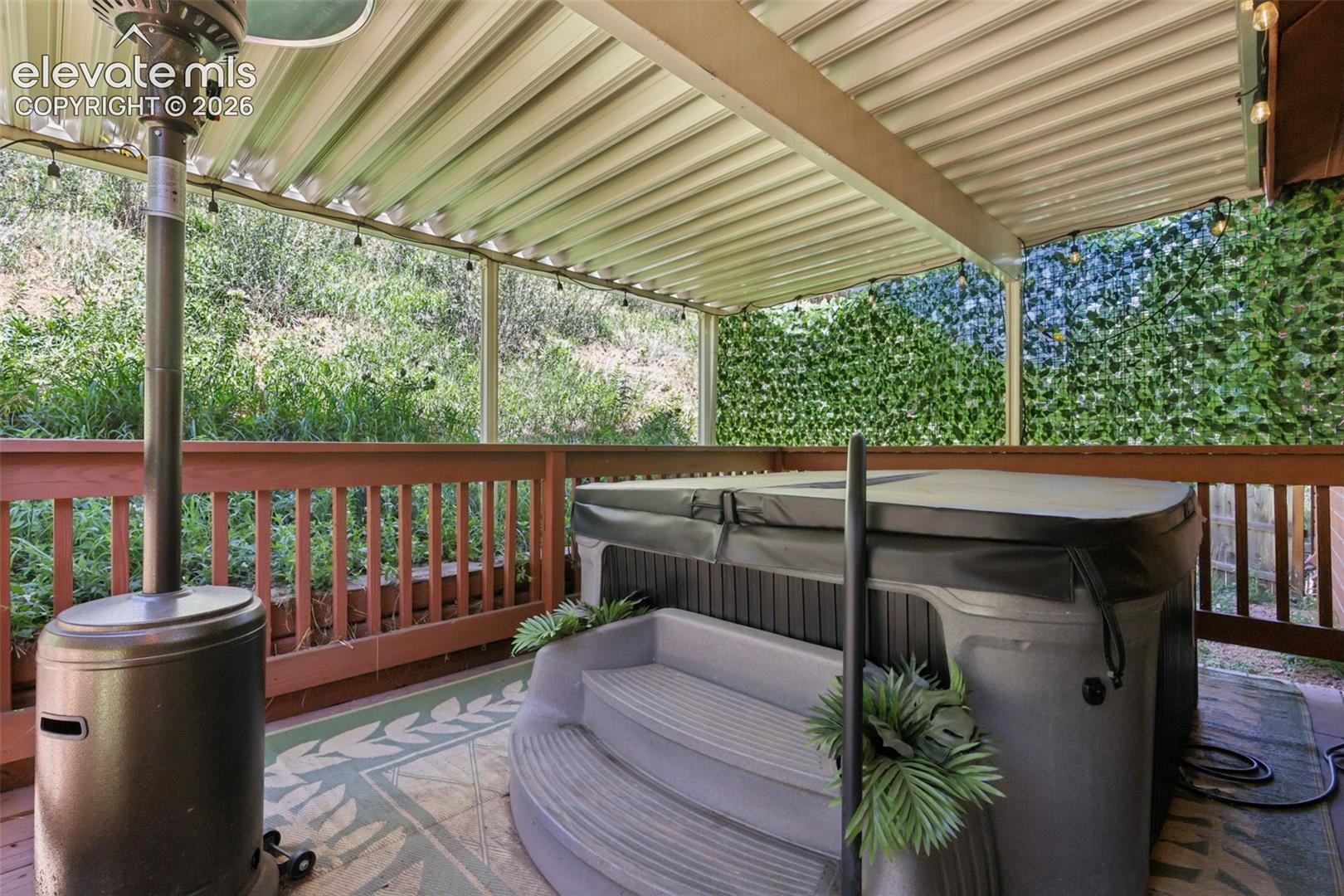 Covered outdoor deck with hot tub, wood railing, and privacy screen