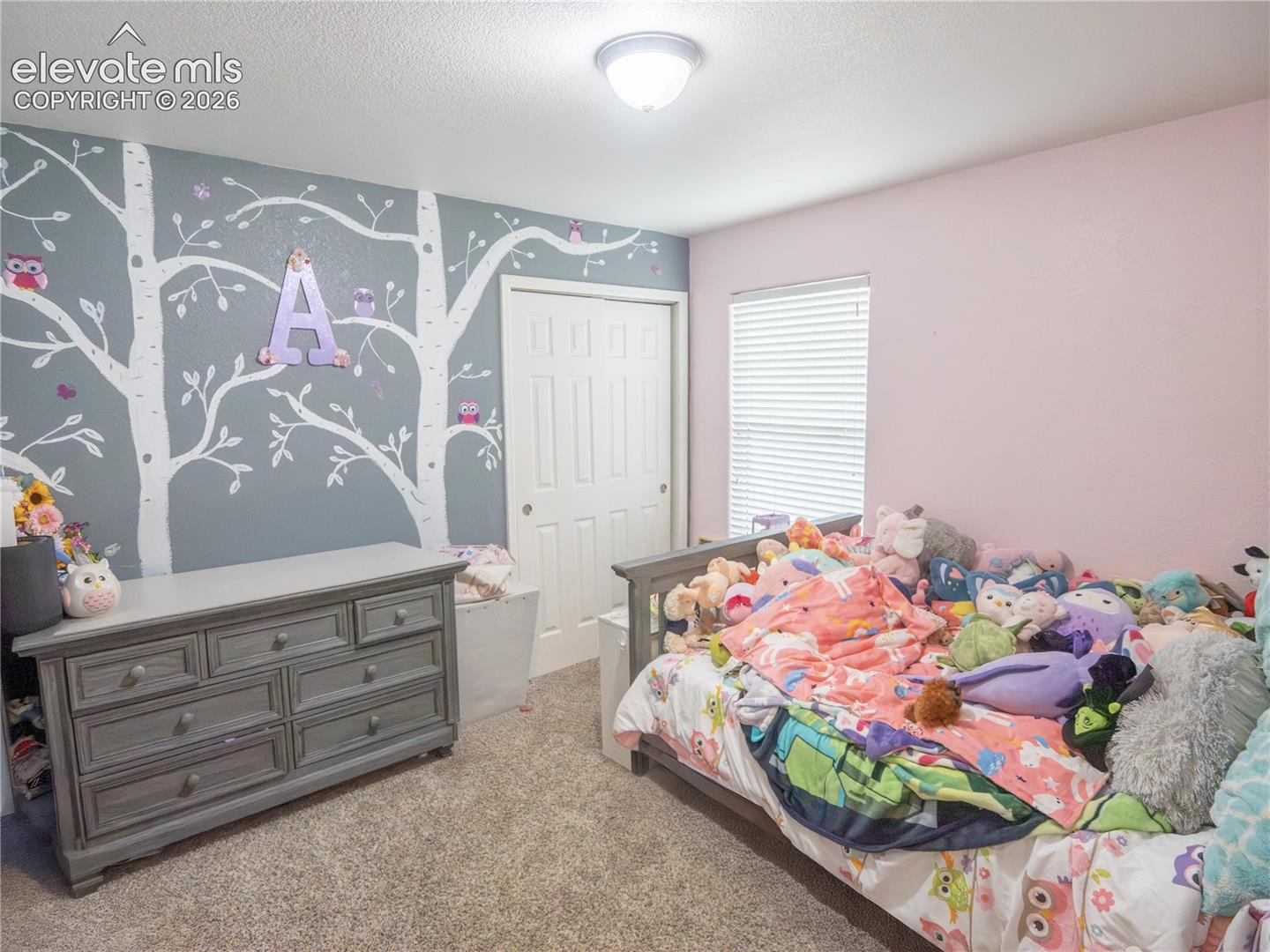 Carpeted bedroom featuring a patterned accent wall and a window with blinds