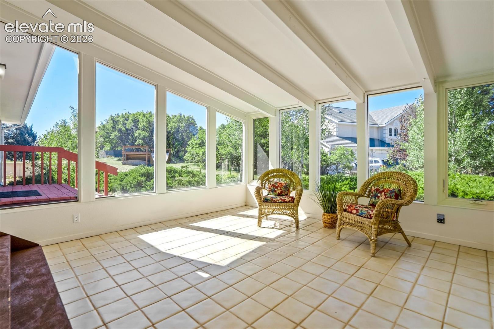Bright sunroom featuring a tiled floor, expansive windows, exposed ceiling beams, and direct access to an outdoor deck with red railings