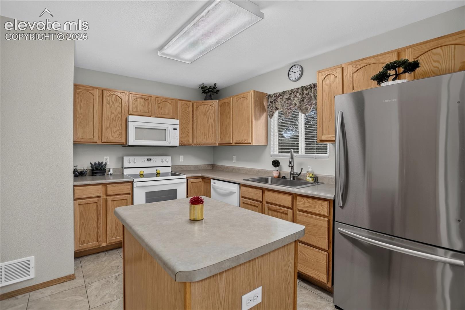 Kitchen featuring wood cabinetry, white appliances, a center island with countertop, and a stainless steel refrigerator
