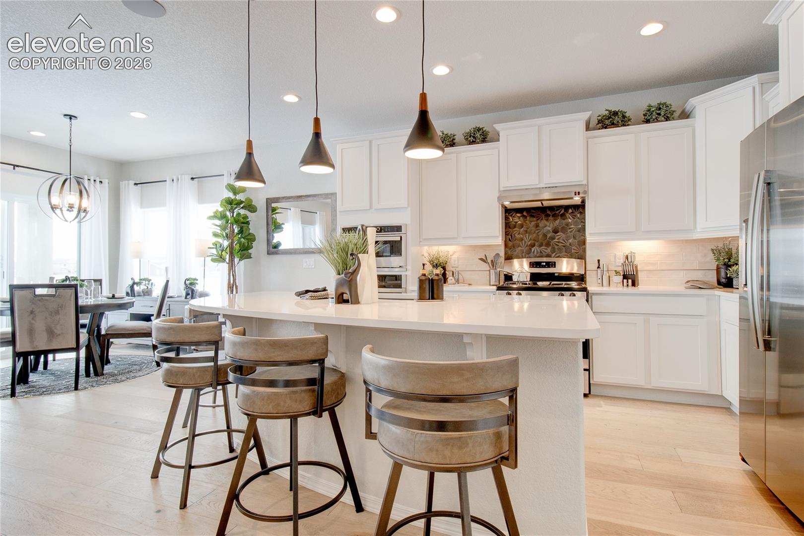 Kitchen featuring a large central island with light-toned countertops, white shaker-style cabinetry, stainless steel appliances, and multi-light pendant fixtures