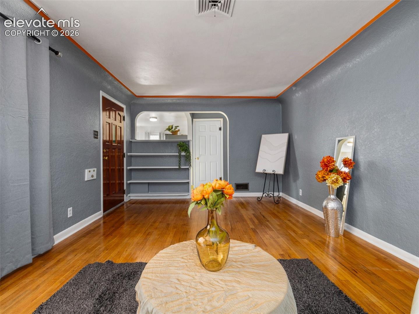 Hardwood flooring, arched wall detailing, built-in shelving, multi-panel entry door, and textured wall finish