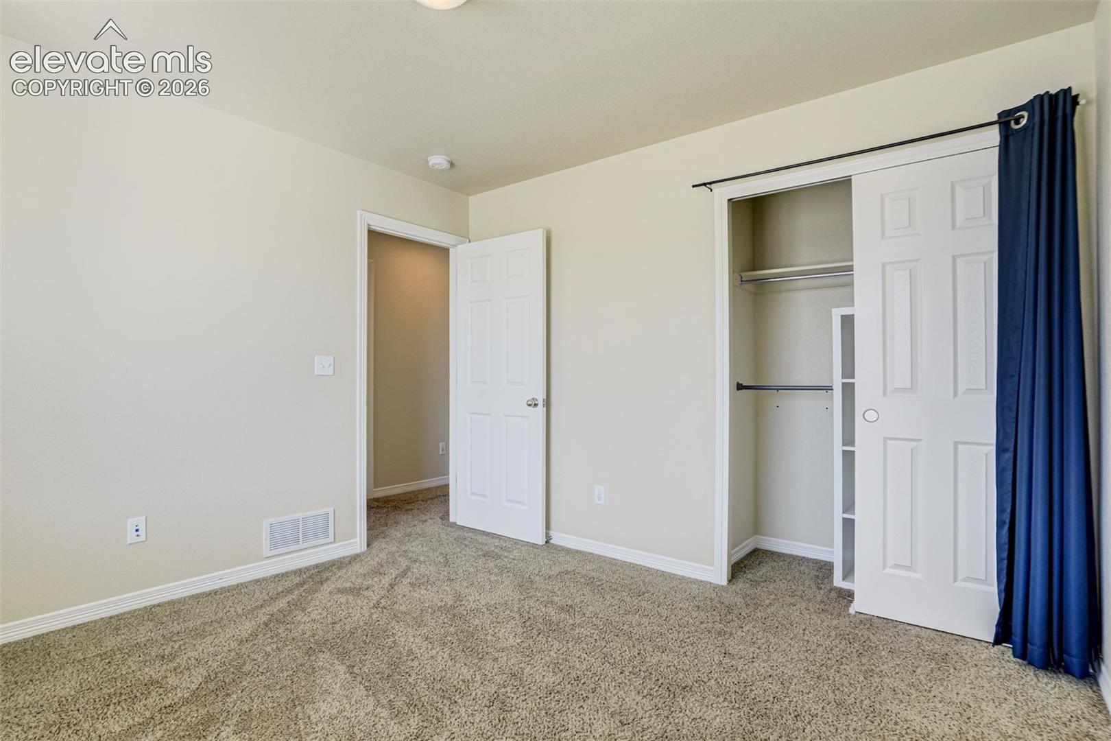 3rd Bedroom with Carpeted flooring with light-toned walls, a white paneled door, and a closet featuring bi-fold doors and built-in shelving