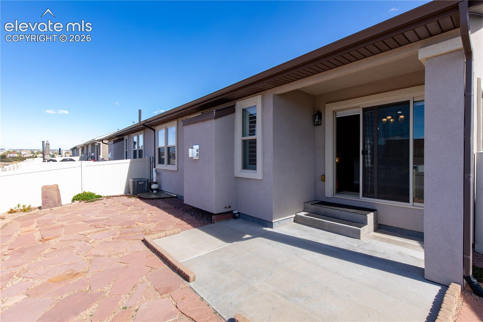 Exterior space featuring a concrete patio, stone paver accents, a covered entrance, and a white privacy fence