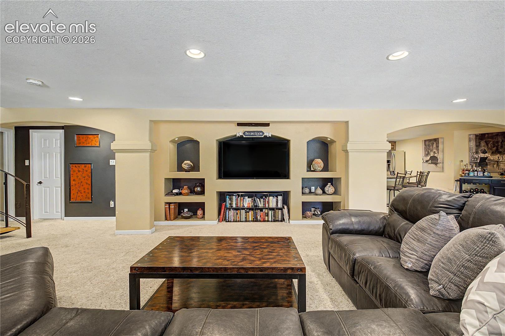 A built-in media wall with arched display niches transforms the lower level into a dedicated space for movie nights and relaxation.