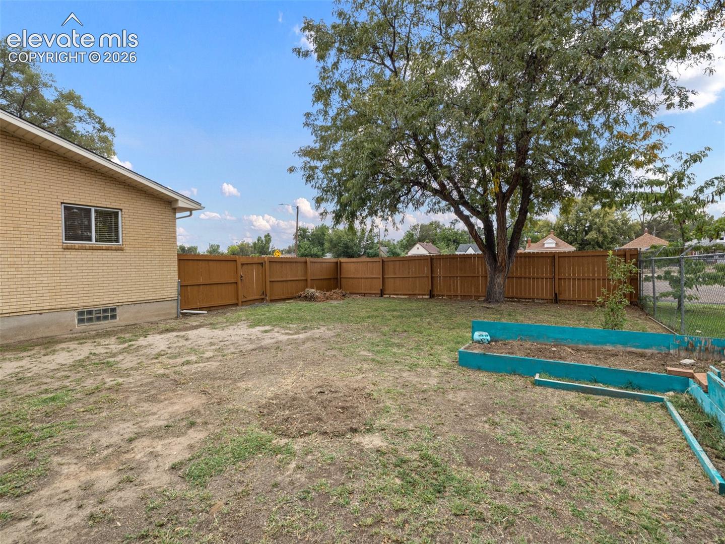 Expansive backyard with a full privacy fence, mature shade tree, and raised garden beds