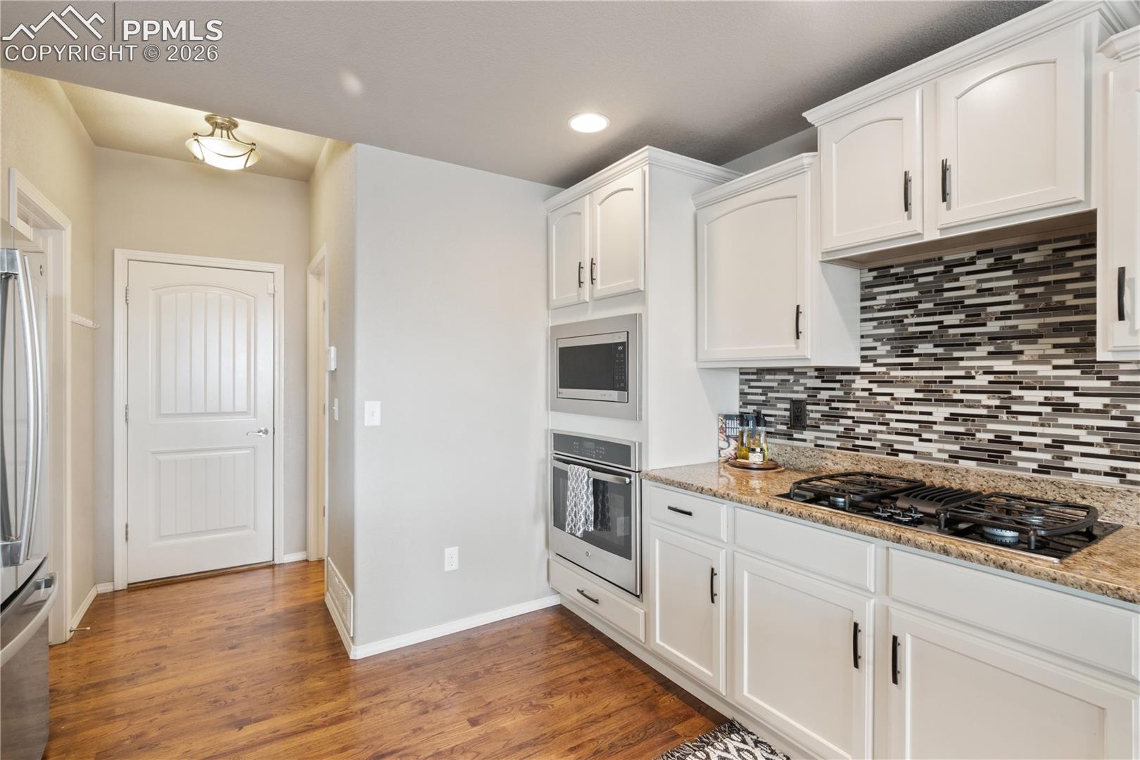 Kitchen featuring stainless steel appliances, white cabinets, light stone countertops, dark wood-style floors, and backsplash