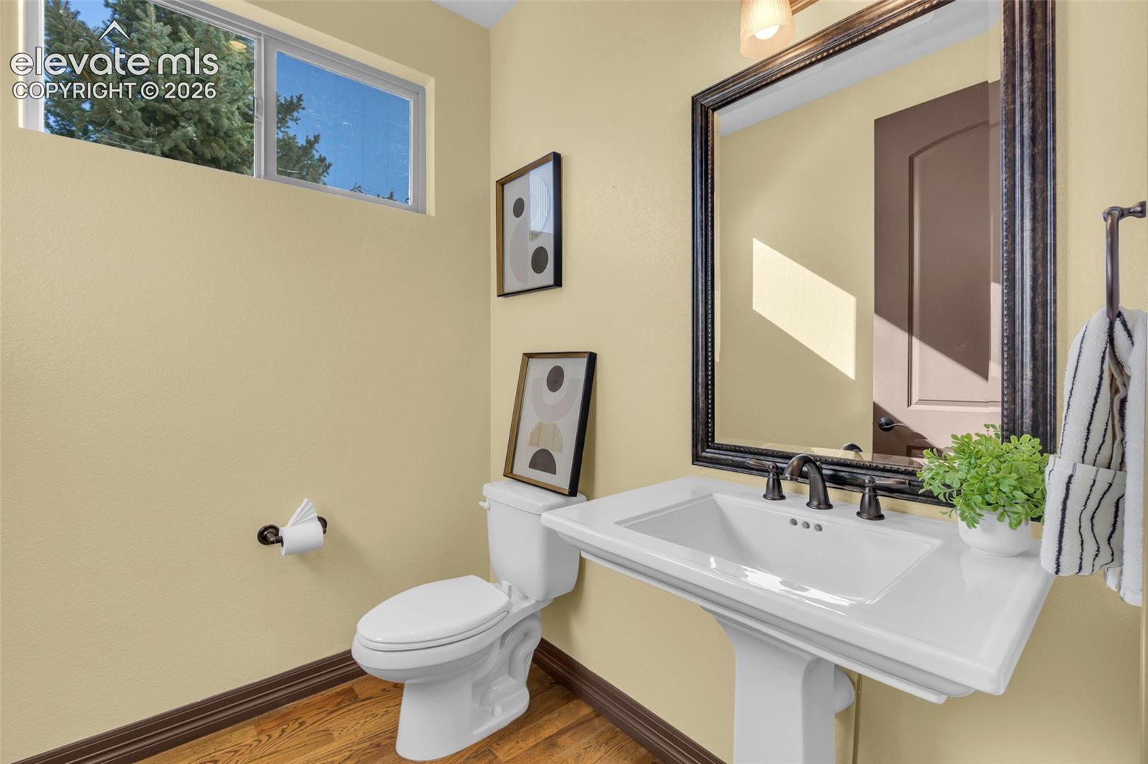 Powder room featuring wood-finish flooring, a white porcelain pedestal sink, widespread oil-rubbed bronze faucet, and a decorative framed wall mirror