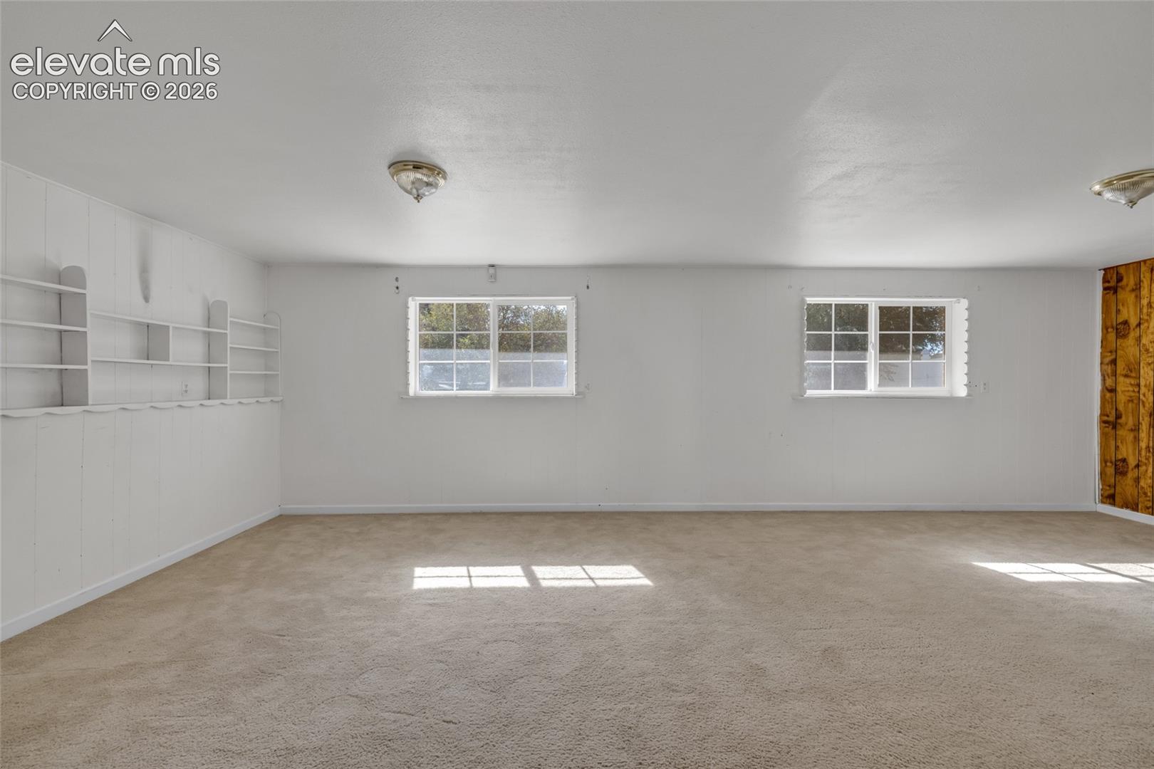 Carpeted flooring with built-in shelving, white paneled wall, and dual windows
