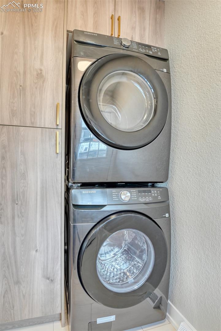 Laundry area with a textured wall and stacked washer and dryer