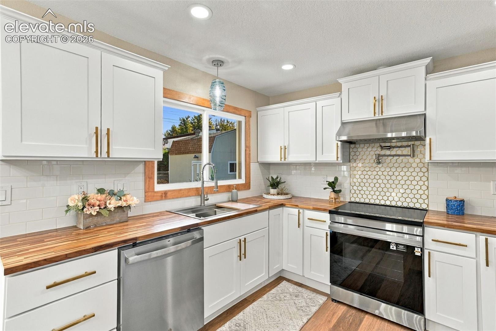 Kitchen featuring white shaker-style cabinetry, wood-finish countertops, stainless steel appliances, a hexagonal tile backsplash, and a wood-trimmed window