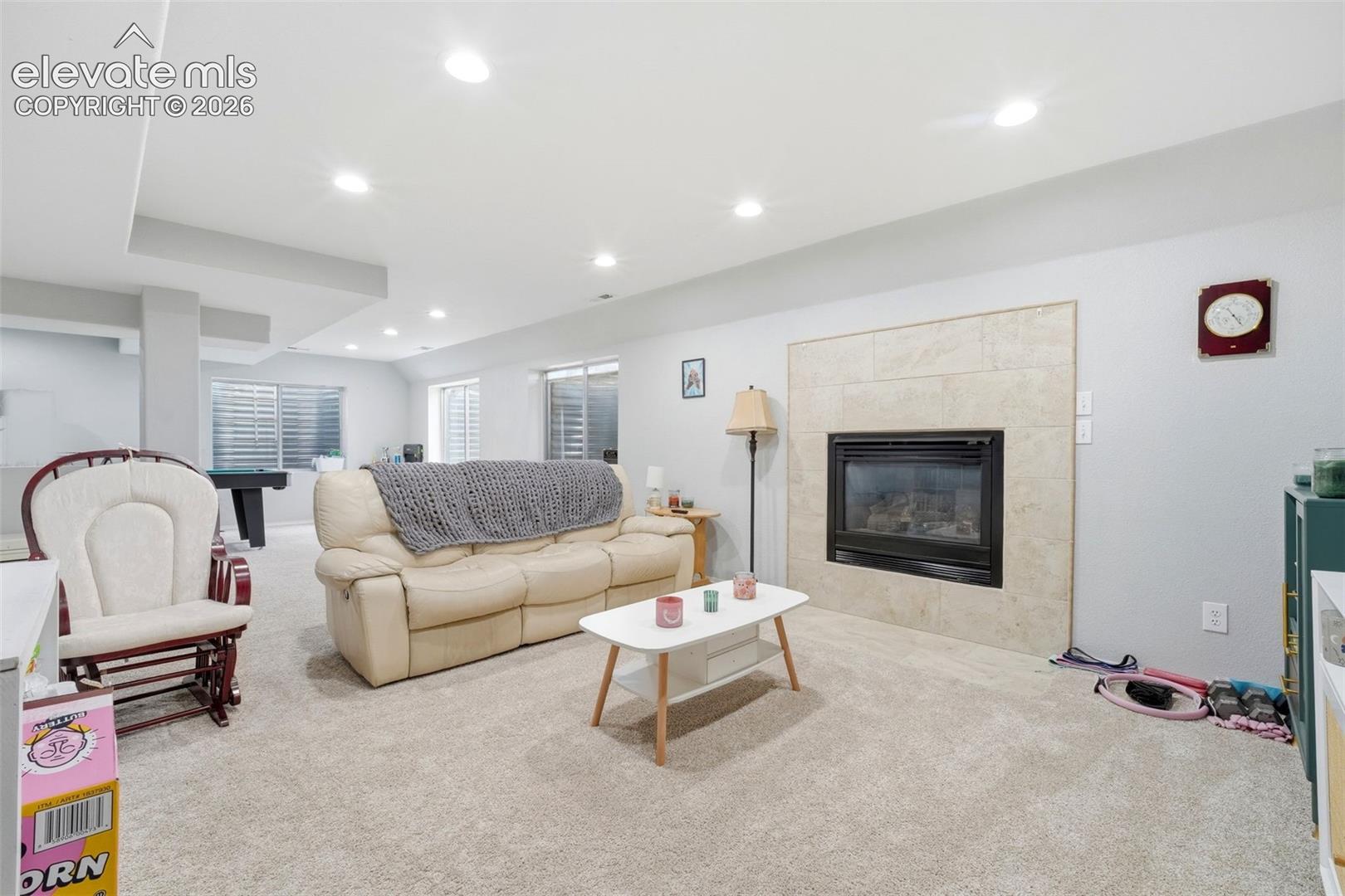 Spacious lower-level living area featuring recessed lighting, light-toned carpeting, and a fireplace with a tiled surround