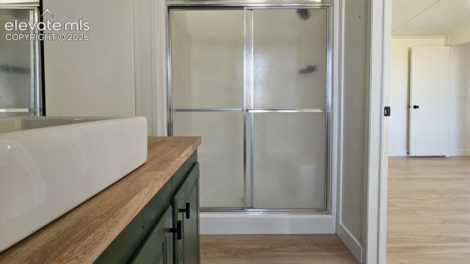 Bathroom featuring a custom cabinet with a natural wood countertop, rectangular vessel sink, matte black hardware, and a glass-enclosed shower