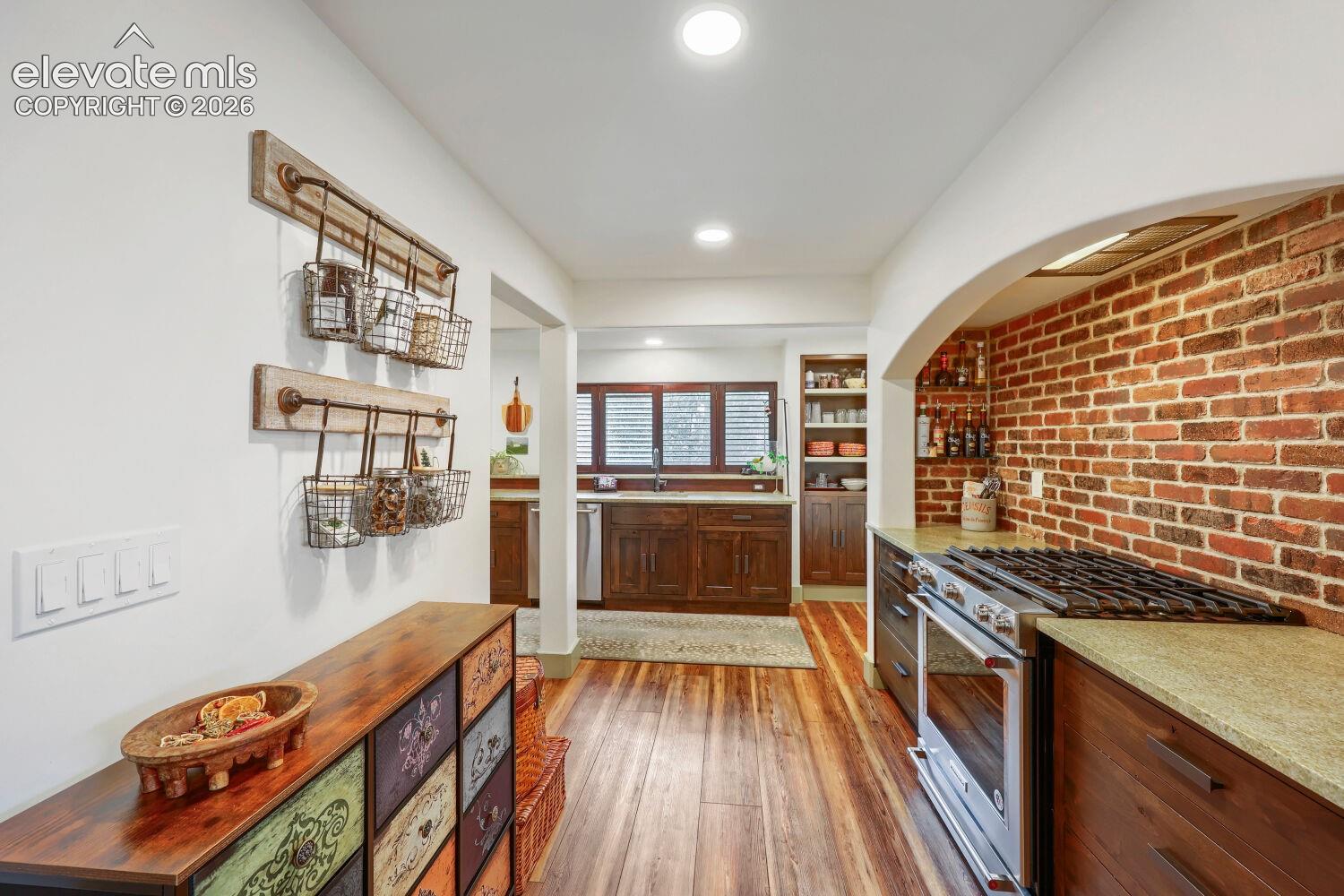 Exposed brick wall detail, hardwood flooring, recessed lighting, built-in cabinetry, and stainless steel range