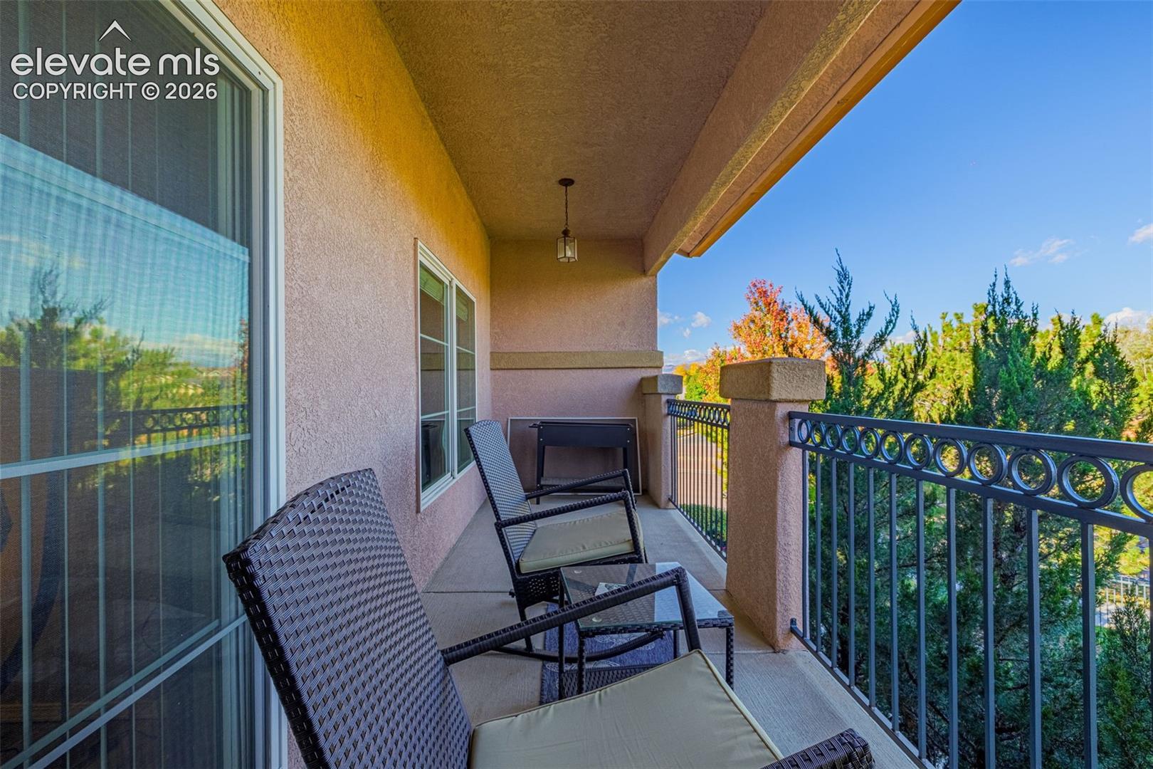 Covered balcony featuring a concrete floor, stucco finish, metal ornamental railing, and ceiling-mounted pendant lighting