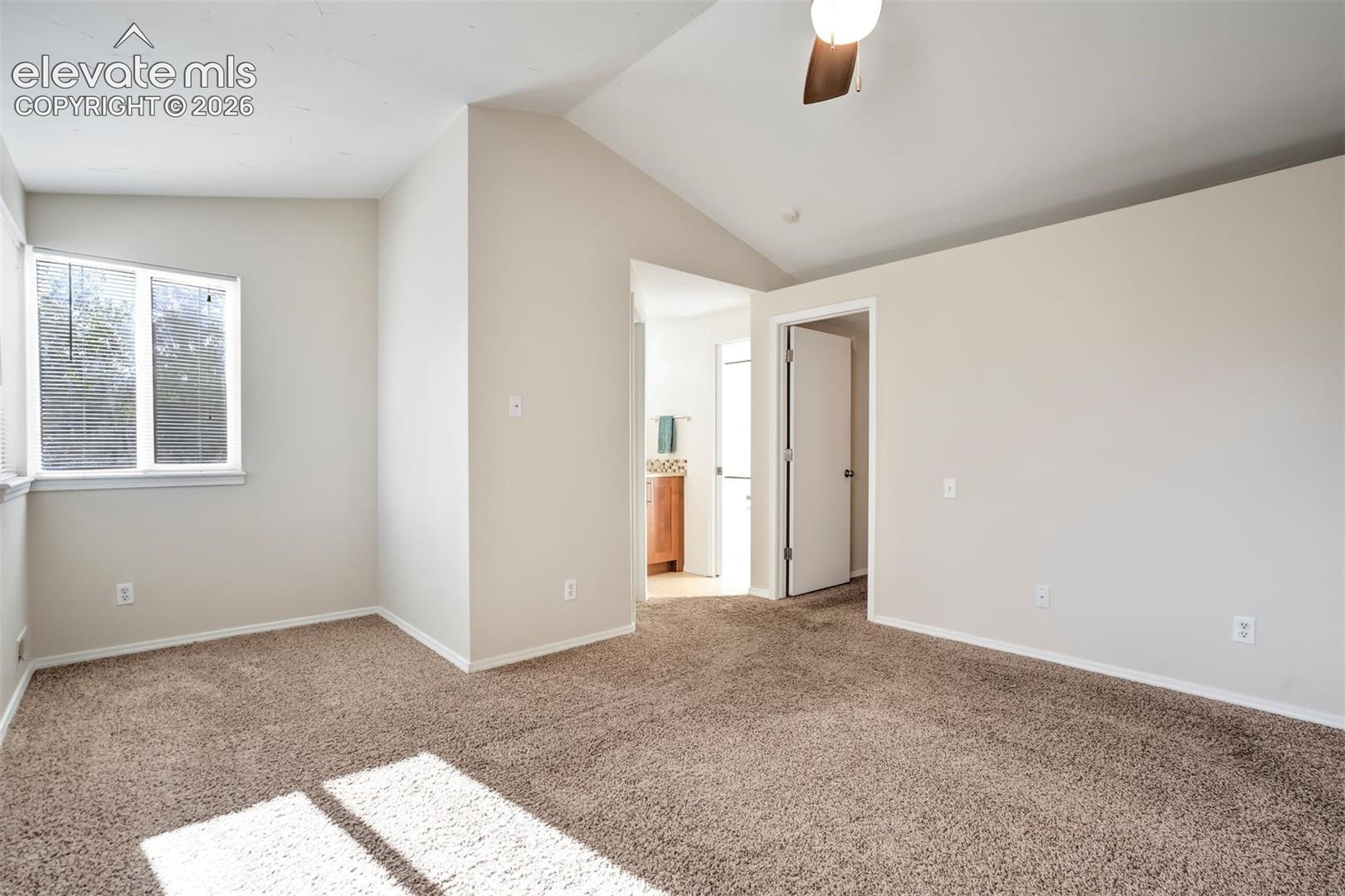 Vaulted ceiling featuring a central light fixture, neutral wall finishes, carpeted flooring, and a window with natural light
