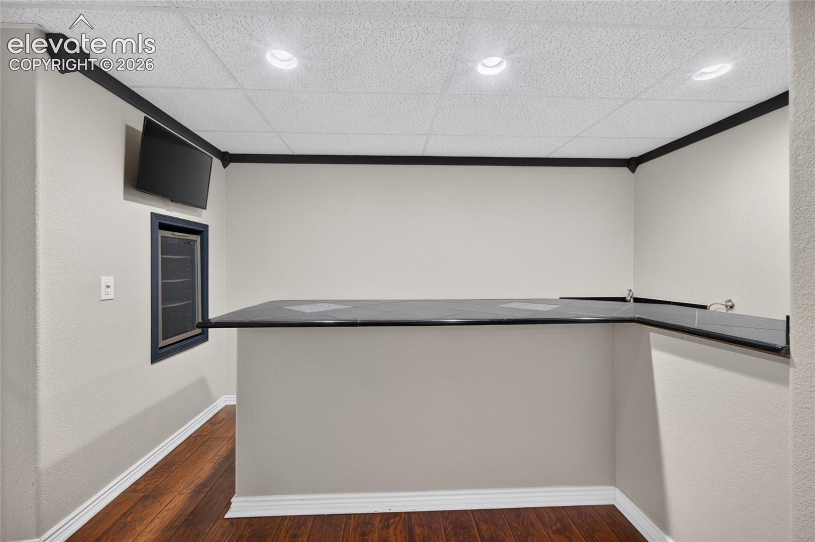 Built-in bar featuring a dark stone-surface countertop, recessed ceiling lighting, wood-finish flooring, and black crown molding