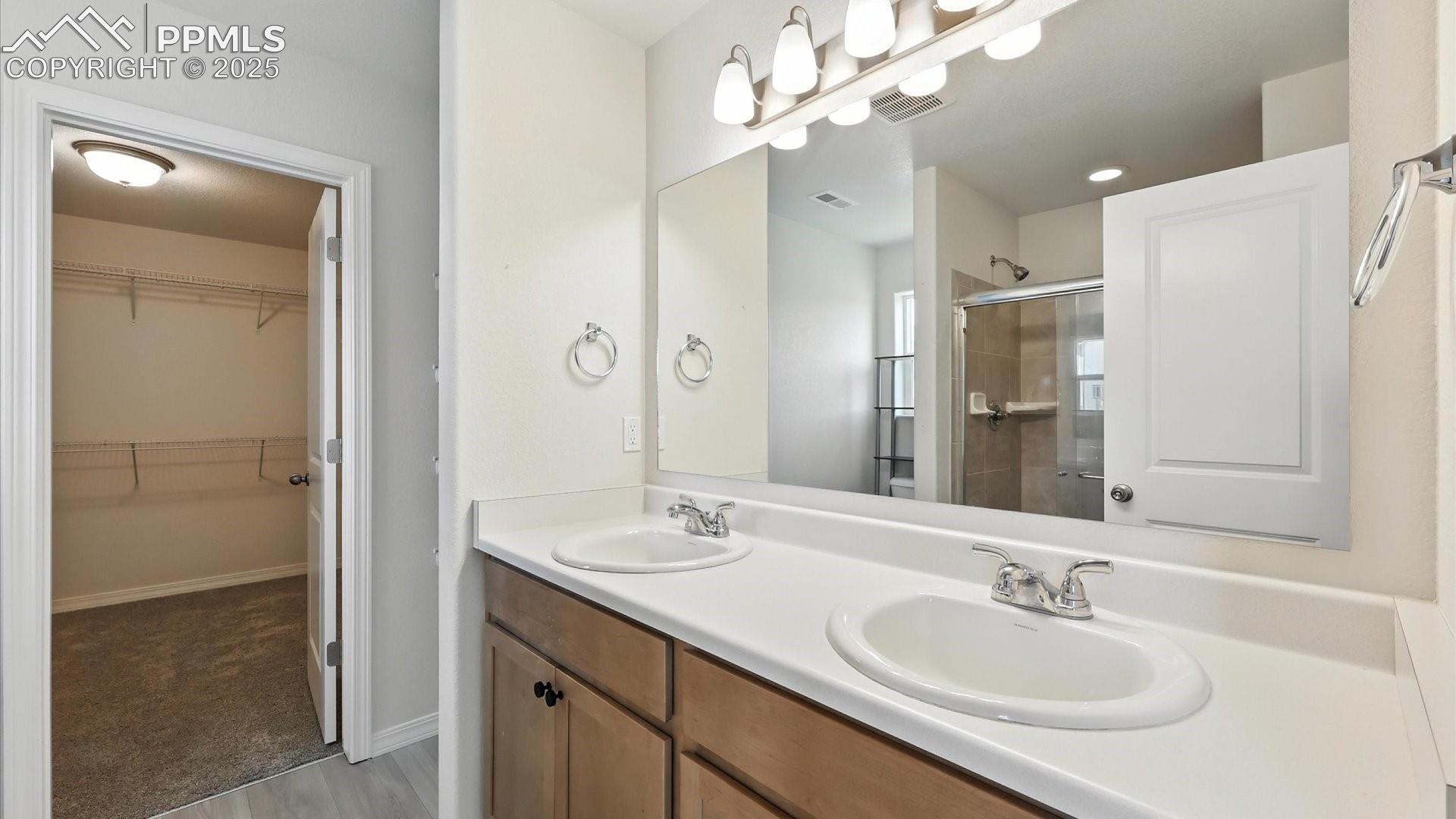 Primary Bathroom with dual sink vanity, tiled shower, and walk in closet.
