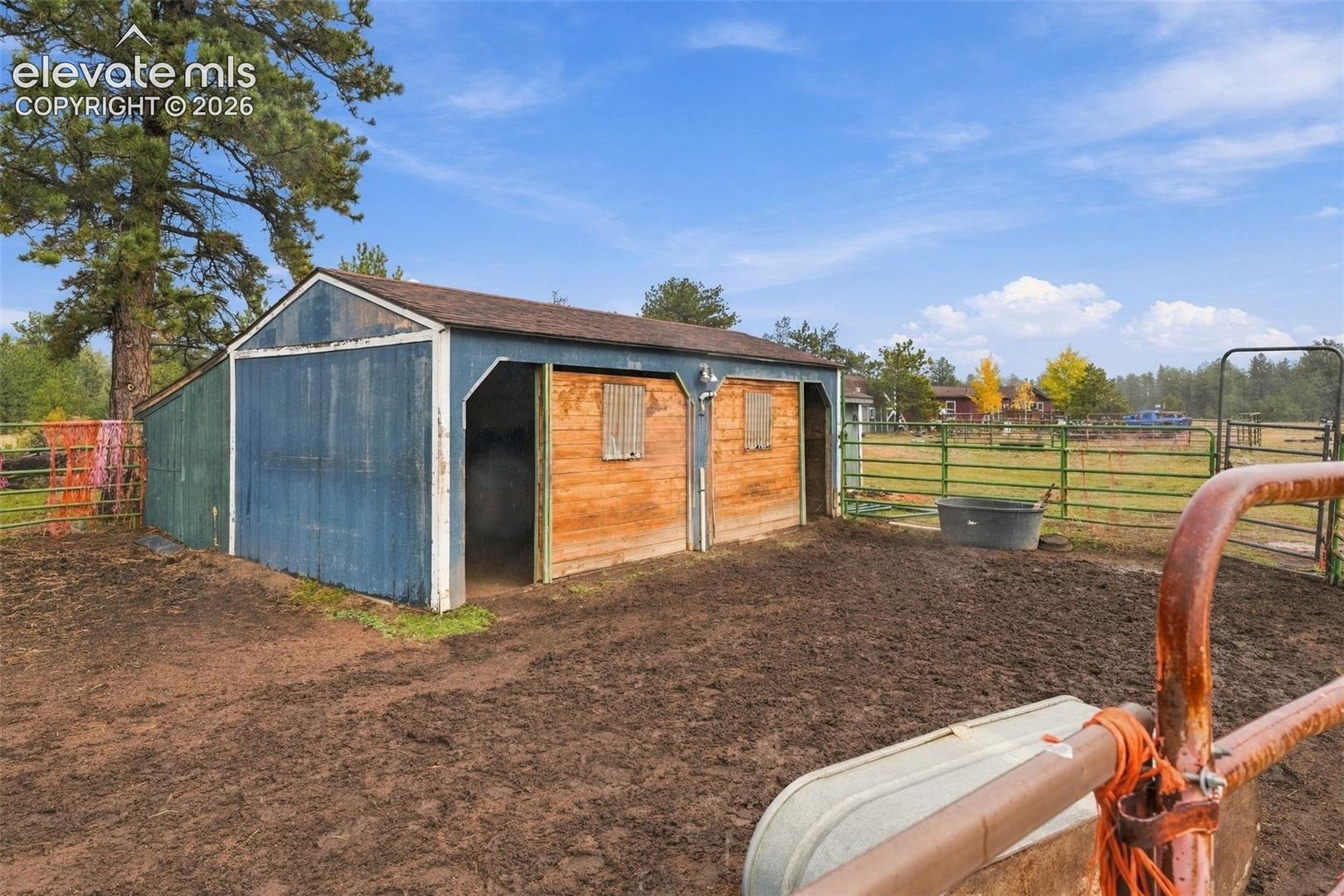 Multi-stall wood-siding barn featuring open-entry bays, metal roofing, and surrounding metal livestock fencing