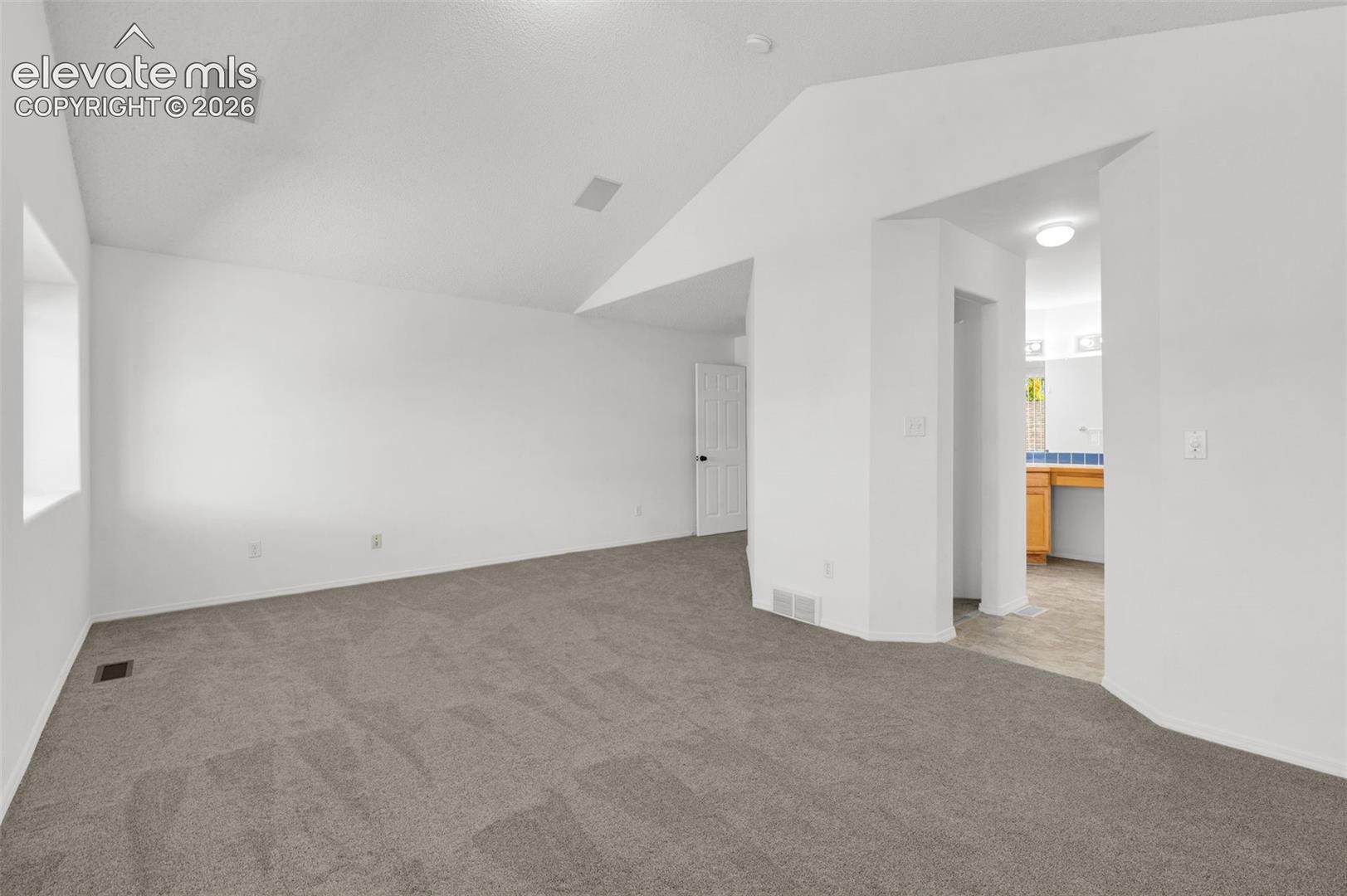 White walls with vaulted ceiling, recessed ceiling speakers, gray carpeting, and a window