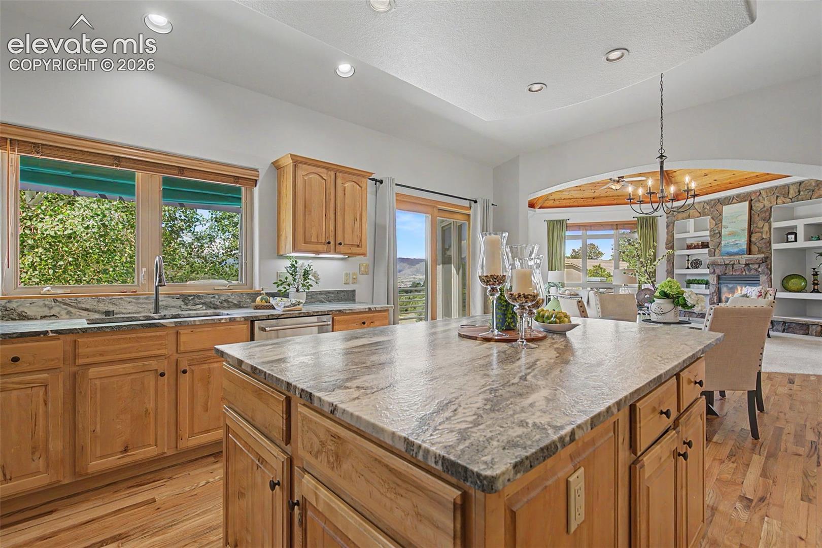 Kitchen featuring an expansive center island with stone-finish countertops, wood cabinetry, stainless steel dishwasher, and wood-finish flooring