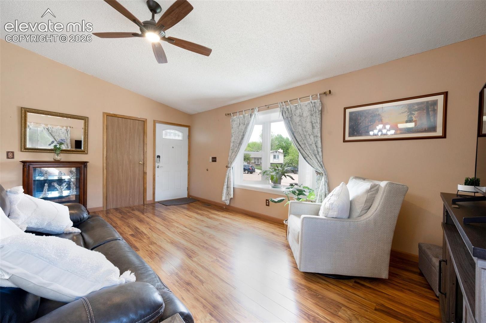 Living area featuring light wood-style floors, vaulted ceiling, ceiling fan, a textured ceiling, and baseboards